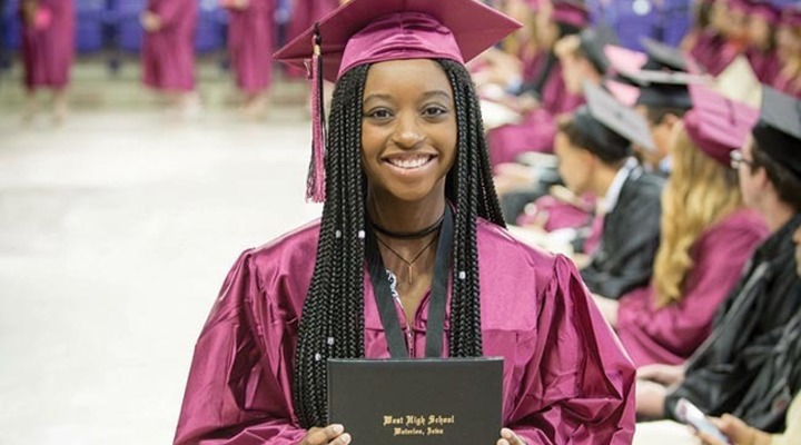 A young black women holds her diploma at graduation.